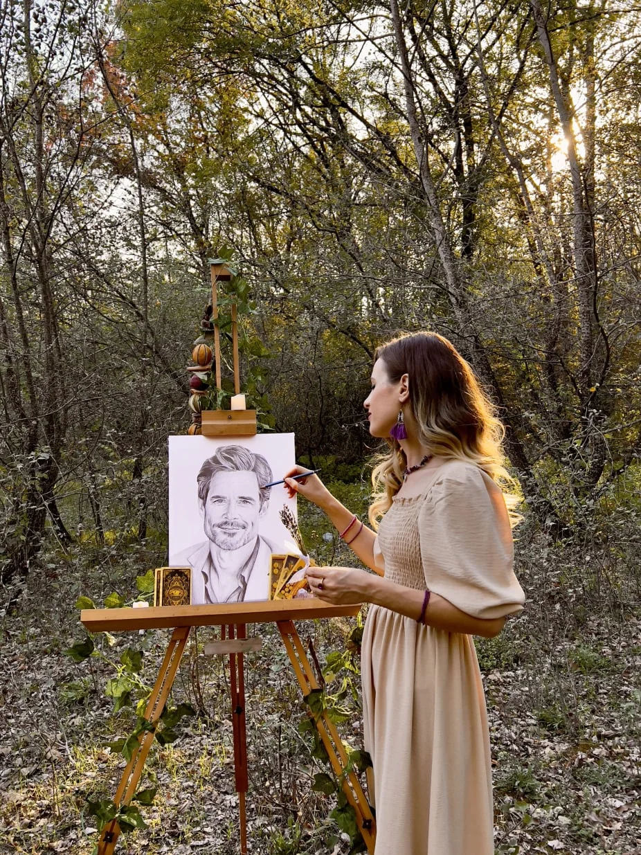 Eva Bloom in nature, hand-drawing a soulmate sketch on her easel in the forest at golden hour